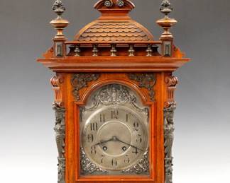 Lot 29: A turn of the century Lenzkirch Bracket clock.  8-day spring driven time and strike movement with Silvered dial and cast spandrels, Arabic numerals, serial #1 Million 309752 indicates a production date of 1901.  Walnut case with cast Brass finials and appliques, upper shingle work crest, Brass gallery over an arched door with figural pilasters and molded base with Brass paw feet.  Older finish with minor wear, running when cataloged.  25 1/2" high overall.  ESTIMATE $800-1,200
