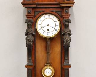 Lot 31: A late 19th century Lenzkirch Model 370 wall clock.  Series 26, 8-day spring driven time only movement with two part porcelain dial, Roman numerals, molded Brass bezel, and gridiron R/A pendulum, serial #212163 indicates a production date of 1871 with Type I trademark.  Figured Walnut case with Ebonized detail features a shaped wooden crest with turned finials over single long door with arched dial glass flanked by Ebonized Spelter Caryatids and composition finials over a shaped lower drop.  Old finish with minor wear, faint hairlines in dial, running when cataloged.  35 1/2" high overall.  ESTIMATE $1,000-1,500  NOTE: This clock is illustrated on page 184 of George Everett's book "Lenzkirch Clocks, The Unsigned Story".
