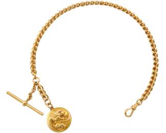 Lot 39: A 14k Gold watch chain with locket.  Ornate double loop T-bar chain with an embossed locket featuring an embossed Dragon with Ruby eye, enclosed four leaf clover.  46.6 grams total weight.  13 3/4" long overall.  Minor wear.  ESTIMATE $2,000-3,000
