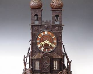 Lot 47: A 19th century Black Forest Monk Bell Ringer table top Cuckoo clock.  8-day time and strike movement with Monk Automaton, Brass cutout plates, silk thread suspension and shield form pendulum, carved wooden dial with bone hands and Roman numerals, half hour strike on two bells with painted Monk bell ringer figure.  Wooden case in the form of an ancient Church with twin upper Bell Towers above a dial surround and lower atrium fitted with glazed windows and Monk's door, all with applied decoration including twigs, roots and bark.  Old finish with minor damage, some glued repairs, running momentarily when cataloged.  28" high overall.  ESTIMATE $2,000-3,000
