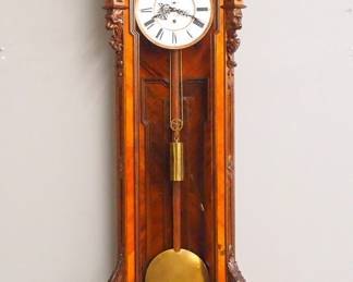 Lot 59: A 19th century Vienna Regulator wall clock by "Anton Lakner, in Wien".  30-day weight driven movement with 10" two part porcelain dial and Roman numerals, fancy filigree hands, subsidiary seconds and Gilded Brass bezel.  Mahogany case with carved crest over a single long door with arched glass, flanked by paneled pilasters with carved detail over a shaped lower drop with carved mask and foliage.  Older refinishing with good color, restored crest and drop, running when cataloged.  77 1/2" high overall.  ESTIMATE $3,000-4,000
