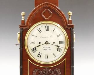 Lot 63: An early 19th century English Regency Period Bracket clock by "Emerson & Co., Bristol, England".   8-day fusee driven time and strike movement with engraved backplate and pendulum, convex painted Iron dial with Roman numerals.  Mahogany case with arched top, Brass flame finial on a gadrooned plinth, arched frieze with applied quatrefoil and Gothic moldings, above a cast Brass dial door and lower inset panel with foliate carving, all flanked by Ebonized triple column pilasters and Brass side handles over inset Brass filigree side panels with Gothic tracery design, on a carved molded base with Brass Lotus feet.  Original finish has been nicely polished with slight wear, correct restored finials, running when cataloged.  21 3/4" high overall.  ESTIMATE $3,000-4,000
