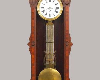 Lot 69: A late 19th century E. N. Welch model "D" wall hanging Jeweler's Regulator.  8-day time only weight driven movement with Pinwheel escapement, porcelain dial with Roman numerals, sweep seconds, molded Brass bezel and bi-metal compensating pendulum.  Victorian Period Black Walnut case in the Eastlake design with hand carved detail features a shaped, scalloped crown with turned finials and carved frieze over a molded cornice and single long door with arched glass shaped frame and applied Burl panels above a tapered drop with applied Burl panel and sawtooth detail.  Brass "Waterbury" plaque added to inside of case. Original finish with some wear and minor damage, one finial with base chip, running when cataloged.  91" high overall.  ESTIMATE $4,000-6,000
