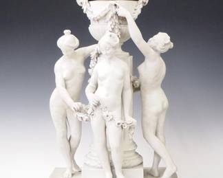 Lot 72: A late 19th century French Three Graces Annular clock.  8-day time and strike movement with platform escapement and dual annular dial rings with porcelain markers, Roman hour numerals and Arabic minutes.  Bisque porcelain case with upper urn and lift off cover and foliate detail, over Neoclassical figures of the Three Graces with floral swags standing before a fluted pedestal on a rectangular plinth with bas relief panels of frolicking Cherubs.  Minor wear, no damage noted, running when cataloged.  24 1/2" high overall.  ESTIMATE S4,000-6,000
