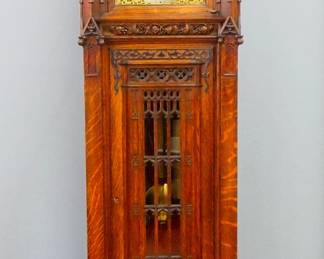 Lot 75: A good late 19th century Waltham Pattern 81 Gothic Revival Period Hall clock.  8-day weight driven movement with quarter hour tubular chimes, Brass dial with painted moon phase, Silvered chapter ring, Roman numerals and subsidiary seconds, "Chime/Silent" and "Whittington/Westminster" selector dials with applied filigree detail.  Exceptional Oak case with carved spires flanking a scrolled crest over a dial door with original beveled glass flanked by Gothic spire pilasters over a waist door with carved tracery and applied Brass detail, lower carved panel and a heavily molded base.  Waxed original finish with minor wear, running when cataloged.  102" high overall.  ESTIMATE $8,000-12,000
