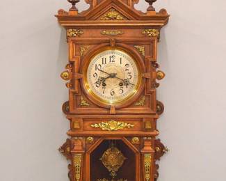 Lot 83: A 19th century Lenzkirch wall clock.  Series 24, 8-day spring driven time and strike movement with etched Silvered dial and Arabic numerals and fancy cast Silvered pendulum, serial #66103 indicates a production date of 1860.  Walnut case with cast Brass decoration, shaped pediment crest over molded crown and single door with circular dial glass and hexagonal lower, above a shaped bracket drop.  Older refinishing with minor wear, running when cataloged.  39" high overall.  ESTIMATE $1,000-2,000
