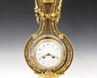 Lot 88: A late 19th century French Gilded Bronze Lyre clock.  14-day time and strike movement with convex porcelain dial, Arabic numerals and hand painted floral swags with Gilded filigree hands, fitted with a gridiron pendulum and swinging exterior bezel decorated with applied "brilliants", serial #205.  White Marble case with Gilded Bronze frame with swags and foliate detail, surmounted by a mask of the Sun God Apollo, on a foliate pedestal and molded Marble base.  Minor wear, hairline free dial, lacks two small medallions at sides of base, movement complete and running when cataloged, set-up and balancing will be required after moving.  22 1/4" high overall.  ESTIMATE $2,000-3,000

