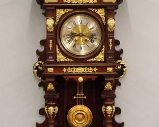Lot 99:  A 19th century Lenzkirch open well wall clock.  8-day spring driven time and strike movement with etched Brass dial, Silvered chapter ring with Roman numerals and fancy embossed Brass pendulum, serial #28647 indicates a production date of 1855.  Walnut case with extensive applied Cast Brass decoration and carved detail, arched crest over molded crown and dial door with circular glass, open well with turned columns over a shaped lower drop.  Older refinishing with minor wear, some restoration, running when cataloged.  48" high overall.  ESTIMATE $1,000-1,500
