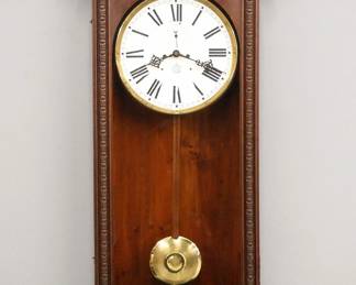 Lot 101: A late 19th century Waterbury No. 67 Regulator wall clock.  8-day dual weight time only movement with dead beat escapement, maintaining power and a papered metal dial with Roman numerals and subsidiary seconds.  Walnut case with a shaped crest and press carved detail over a single molded door and shaped bracket drop.  Paper label 60% intact at bottom.  Older refinishing with minor wear, restored dial and drop, running when cataloged.  49" high overall.  ESTIMATE $1,000-1,500
