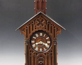 Lot 102:  A 19th century Black Forest Monk Bell Ringer table top Cuckoo clock.  8-day time and strike movement with Brass cutout plates, turned wooden dial with carved bone hands and Roman numerals, "Bim-Bam" strike on two bells with painted monk bell ringer figure.  Oak Gothic Revival Period case with extensive carved detail including a upper Bell Tower with tapered finial above a dial surround with carved tracery flanked by Ebonized pilasters on a molded base with pierced cutouts.  Old dark finish with some glued repairs, crack in base, lacks roof trim, running momentarily when catalogued.  34 3/4" high overall.  ESTIMATE $1,000-1,500
