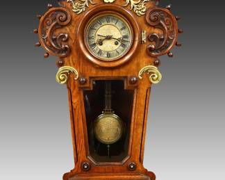 Lot 118:  A late 19th century German carved Oak wall clock with applied chased Bronze decoration, in the style of Lenzkirch.  8-day spring driven time and strike movement with a Silvered dial and Roman numerals, etched dial center with foliate design in Gold and Silver detail with matching compensating pendulum.  Oak case with lift-off facade having an arched crest with two carved finials supported by turned columns, turned Oak bezel flanked by foliate carvings and Brass finials over a beveled glass panel and pierced carved drop with applied Bronze Angel and foliate wreaths, terminating in a carved Shell form drop finial.  Serial #"52183" on back plate.  Nicely restored finish, some loss and cracks in Bronze work, corner damage on beveled glass, running when cataloged.  40" high overall.  ESTIMATE $1,000-1,500

