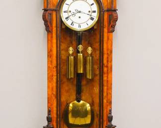 Lot 133:  A late 19th century Vienna Regulator wall clock.  8-day weight driven time and strike movement with quarter hour Grand Sonnerie chime and two part porcelain dial with Roman numerals and molded Brass bezel.  Transitional Figured Walnut case with Ebonized detail features a carved crest and arched molding over a single long door with arched glass flanked by chamfered pilasters with carved detail over a shaped drop.  Older finish with some wear and minor damage, replaced crest, dial hairlines, mis-matched weights, running when cataloged.  47" high overall.  ESTIMATE $600-800
