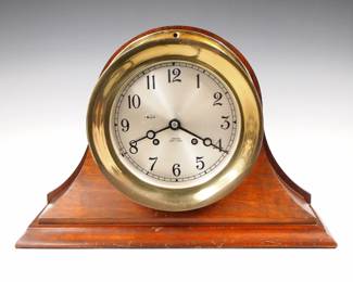 Lot 134: A mid 20th century Chelsea "Ship's Bell" model ship's clock.  8-day time and strike movement with balance wheel escapement strikes on ship's bells with a 6" Silvered dial and Arabic numerals with strike/silent lever.  Serial #554260, ca. 1944-5.  Brass case with hinged bezel, on a Mahogany stand.  Includes the original "Chelsea" winding key.  Some wear and light surface corrosion to Brass, running when cataloged.  9 1/2" high overall.  ESTIMATE $800-1,200
