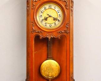 Lot 150: A turn of the century Matthais Bauerle wall clock (with "MANN" trademark).  8-day spring driven time and strike movement with etched Brass dial, porcelain chapter ring with Arabic numerals and etched Brass pendulum, serial #90305.  Second Baroque Period Walnut case with carved decoration, shaped crest over molded crown and single long door with circular dial glass and shaped lower above a shaped drop.  Older refinishing finish with minor wear, some shrinkage to door frame, minor loss to top carving, running when cataloged.  36" high overall.  ESTIMATE $600-800
