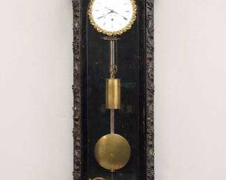 Lot 151: A turn of the century Miniature Vienna wall clock by Karl Ludwig, Pressburg.  8-day weight driven time only movement with a 4 1/4" flat porcelain dial and Roman numerals and Cast Piecrust bezel.  Ebonized wood case with shaped metal crest over an arched door with composition pilasters and shaped lower drop.  Old finish with minor wear, replaced crest, hairlines and small flake in dial, running when cataloged.  27 1/2" high overall.  ESTIMATE $600-800

