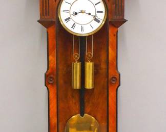 Lot 158: A late 19th century Lenzkirch wall clock.  8-day weight driven time only movement with two part porcelain dial, Roman numerals, molded Brass bezel, serial #220346 indicates a production date of 1871 with Type I trademark.  Walnut case with Ebonized detail features a shaped wooden crest with carved Eagle and arched moldings over single long door with arched dial glass, short fluted pilasters and shaped frame with carved Oak leaves over a shaped lower drop.  Older finish with minor wear, faint hairlines in dial, some restored carvings, running when cataloged.  50 1/2" high overall.  ESTIMATE $600-800
