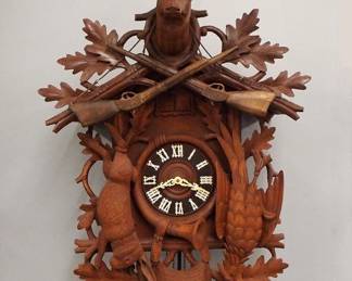 Lot 163: A late 20th century German Black Forest musical Cuckoo wall clock.  30-hr three weight movement with Brass cutout plates, cuckoo and musical chime at the hour and half, turned wooden dial with applied Roman numerals.  Carved mixed wood case with hunting motif features a Stag head finial, over a crest with Oak leaves and rifles, above hanging game and various hunting accoutrements.  Some surface wear, glued repairs to crest, mis-matched weights, running when catalogued.  41" high plus weight drop.  ESTIMATE $600-800
