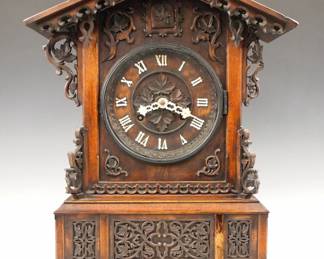 Lot 168:  A 19th century Black Forest table top Cuckoo clock.  8-day double fusee time and strike movement with wooden plates, carved dial and applied bone hands and Roman numerals.  Walnut Gothic Revival Period case with extensive carved detail including an arched crest above a dial surround with carved tracery flanked by rope twist columns on a stepped base with molded feet.  Older finish with some wear, minor damage, lacks roof trim and one side door, added dial door, running when cataloged, Cuckoo needs adjustment.  19 3/4" high overall.  ESTIMATE $600-800
