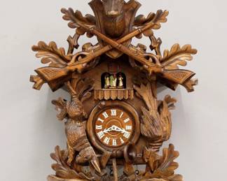 Lot 181:  A late 20th century Black Forest Cuckoo wall clock by Anton Schneider & Sohne.  30-hr three train weight driven time and strike movement with music box and automaton, wooden dial with applied Roman numerals.  Carved mixed wood case with Stag and Rifle crest, dancing figures and hanging game at dial, Oak leaves and hunting accoutrements.  Original finish with slight wear, running when cataloged.  32" high plus weight drop.  ESTIMATE $600-800
