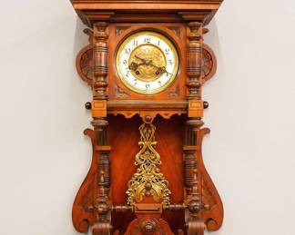 Lot 187:  A turn of the century German open well wall clock by Carl Werner (with Konkurrenz "Horseshoe" trademark).  8-day spring driven time and strike movement with embossed Brass dial, porcelain chapter ring with Arabic numerals and fancy Brass pendulum.  Walnut case with applied Cast Brass decoration, gallery crest over molded crown and dial door with circular glass, open well with turned posts and lower bracket drop.  Original finish with minor wear, running when cataloged.  40" high overall.  ESTIMATE $400-600
