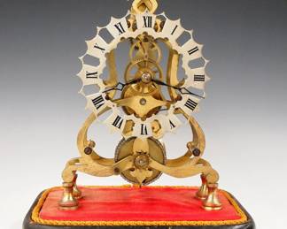 Lot 192:  A turn of the century English Skeleton clock.  8-day time only chain driven fusee movement with Silvered filigree dial and Roman numerals.  Shaped Brass plates with "Fleur-di-Lis" detail and turned posts, on a molded wooden base with painted Black finish.  Minor wear, lacks dome, running when cataloged.  14" high overall.  ESTIMATE $400-600
