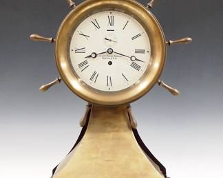 Lot 198:  A 20th century "U. S. Life-Saving Service, Boston, U.S.A." mantel clock.  8 day time only movement with platform escapement, papered metal dial, Roman numerals and subsidiary seconds.   Brass case with upper Ship's Wheel bezel and shaped Brass plinth on a painted wooden base.  Some dents in Brass case, running when cataloged.  22 1/2" high overall.  ESTIMATE $400-600
