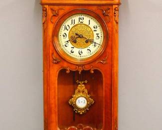 Lot 207: A turn of the centaury Gustav Becker wall clock.  8-day spring driven time and strike movement with an embossed Brass dial and porcelain chapter ring with Arabic numerals cast gridiron R/A pendulum, serial #1282112.  Second Baroque Style Walnut case with carved crest over a single long door with circular dial glass and shaped lower over a shaped drop.  Married movement and case, older refinishing with some wear and minor damage, restored crest and bottom finial, running when cataloged.  40" high overall.  ESTIMATE $200-300
