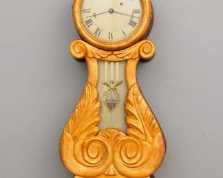Lot 225:  A reproduction Boston style Lyre front Banjo clock.  8 day weight driven time only movement with a painted Iron dial and Roman numerals.  Mahogany case with Gilded decoration, Eagle finial over a circular dial door with convex glass and foliate carved throat panel with reverse painted glass, shaped drop with carved finial.  Finish and dial have been poorly "antiqued", running when cataloged.  38 1/2" high overall.  ESTIMATE $600-800

