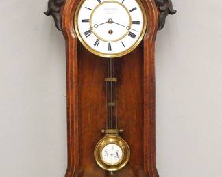 Lot 228: A late 19th century German RA wall clock by Gustav Rost, Dresden.  8-day spring driven time only movement with two part porcelain dial, Roman numerals and gridiron RA pendulum, serial #11635.  Walnut case with Ebonized detail, shaped top with turned finials over single door with molded frame and carved detail, shaped drop and turned finial.  Older finish with some wear, flake in pendulum bob, running when cataloged.  37" high overall.  ESTIMATE $300-400

