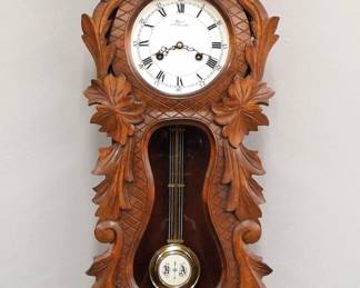 Lot 235:  A 20th century Wuersch wall clock.  8-day spring driven time and strike movement with painted metal dial, Roman numerals marked "Wuersch, Fall River Mass".  Walnut case with a single long door, carved overall with flowers and foliate scrolls, circular dial glass and shaped lower.  Minor wear, running when cataloged.  29 1/2" high overall.  ESTIMATE $200-300 
