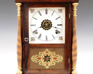 Lot 250: A late 19th century Gilbert Cottage clock.  8-day time and strike movement with alarm, papered metal dial and Roman numerals (includes the original painted metal dial with flaking).  Rosewood case with molded crown over a single door with clear dial glass and reverse painted lower flanked by turned columns on a molded base.  Old finish with minor wear, re-papered dial, running when cataloged.  15" high.  ESTIMATE $200-300
