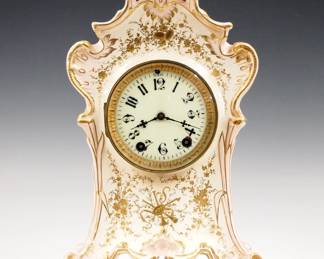 Lot 255: A turn of the century Seth Thomas China shelf clock.  8-day time and strike movement with Brass bezel, porcelain dial and Arabic numerals.  Porcelain case in Art Nouveau style with Pink highlights and Gilded floral decoration.  Minor wear and crazing, hairline in case back, running when cataloged.  13 3/4" high overall.  ESTIMATE $100-150
