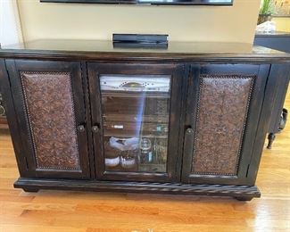 Hooker Furniture Distressed Media Cabinet - 59” wide x 23” deep x 36” high.  Two decorative doors with enclosed storage.  Middle door is glass.  Has vents and cutouts for wiring.  Black distressed with brown tones running thru it.  