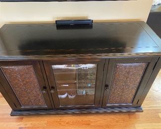 Hooker Furniture Distressed Media Cabinet - 59” wide x 23” deep x 36” high.  Two decorative doors with enclosed storage.  Middle door is glass.  Has vents and cutouts for wiring.  Black distressed with brown tones running thru it.  