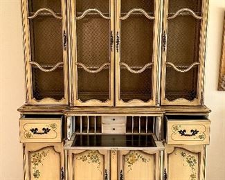 Vintage Stunning  2pc China/Display Hutch by Saginaw Furniture with Wire Mesh on doors and painted in a buttery antique paint (original) with Floral Stencils on Doors and Drawers.  This piece morphs into a secretary, as the center opens out into a desk,  Super impressive Piece from the 1960's and it's oh so cool!