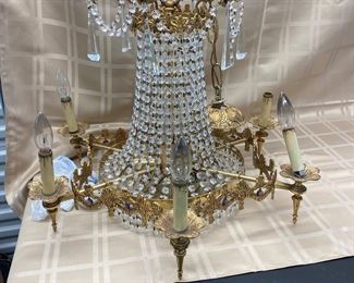 LOT 021- Marked "MADE IN SPAIN" Hollywood regency chandelier in the style of Swarovski AS-IS. There are bent sockets, damage to the metal at the sockets and prism loss. $575 