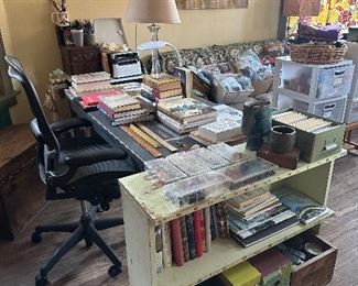 Craft room. Full of books, supplies, knitting, supplies, crocheting, supplies, lamps, art maps, clothing.