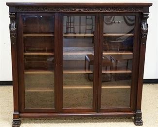 1118	MAHOGANY TRIPLE DOOR BOOKCASE W/CARVED WINGED GRIFFINS & PAW FEET, ONE DOOR GLASS REPLACED W/PLEXI, APPROXIMATELY 69 IN X 17 IN X 63 IN HIGH
