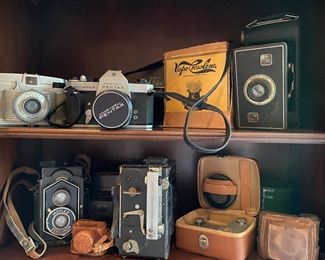 In bottom left corner: Ikoflex 850/16 Often referred to as the "coffee can" or "original", this camera is styled with film counters for 120 and 620 film. Lever focus at bottom front of the camera. Early models have an art deco hood, while the later models are covered with leather. Lenses are Novar 4.5 or 6.3 in Derval, Klio or Compur-Rapid shutters. 1934-37.