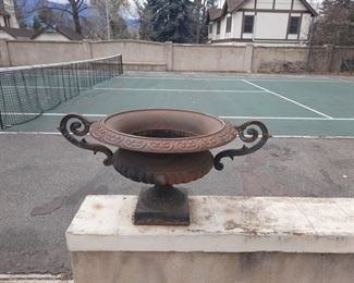 Cast metal urn (1 of 2) in front of backyard tennis court .