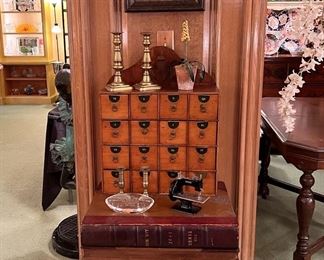 Antique apothecary cabinet with lettered drawers, antique English brass candlesticks, miniature working Singer sewing machine, majolica planter, table made from actual “English Times” 1897 newspapers