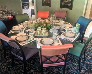 This round glass top table seats eight people; the chairs are upholstered as pairs in jeweled toned fabric.