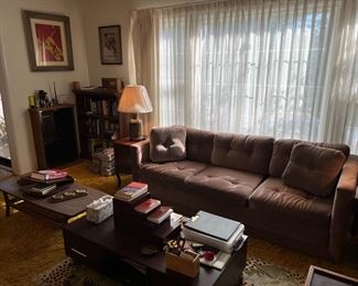 A grand picture of the living room. Notice the sofa, tables, bookcases, artwork, and more.
