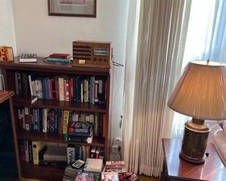 A close-up picture of the living room corner, with a bookcase, side table, lamp, books, CDs.
