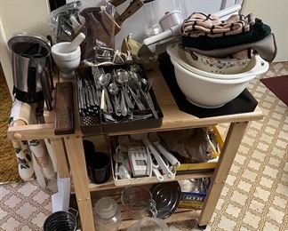 This rolling cart is holding bowls, silverware, a knife rack, and various other kitchenware items.