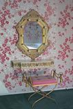 A wall mounted vanity table, complete with lighted mirror and a gilded iron Roman style bench with cushioned seat.