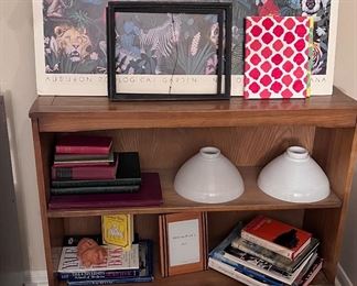 Vintage wooden book shelf with wheels holding lots of books and 2 milk glass light globes