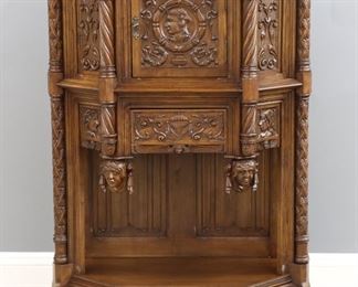 An early 20th century French Gothic Revival Period carved side cabinet.  Oak construction with a shaped molded top over a central door with carved portrait panel flanked by turned columns with mask pendants and carved foliate panels, a single dovetailed drawer and an open lower shelf with linen fold back panels on a simple molded base with block feet.  Restored finish with slight wear.  40 x 19 x 59" high overall.