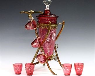 Six pieces of late 19th century Cranberry glass drinkware.  Enameled floral decoration with Gilded detail.  Includes a pitcher with ruffled rim and a carafe with four matching glasses.  Some surface wear and minor losses to Gilding, a few tiny flakes at rims, carafe with production flaw at neck.  Up to 9 1/4" high.  
