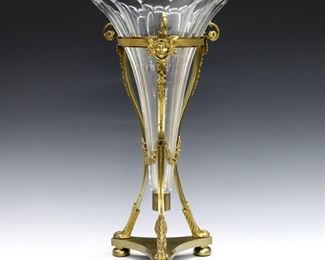 A turn of the century French Louis XVI style Bronze and Crystal vase.  Neoclassical Gilt Bronze frame on three paw feet and tripod base, holding a faceted Crystal trumpet vase with scalloped rim.  Some wear, flakes to crystal rim, one repaired Bronze scroll.  16" high.  